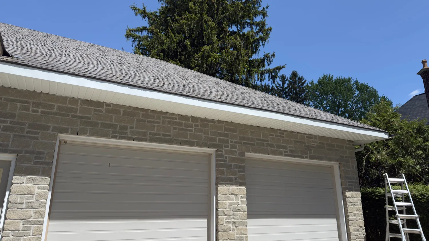 Finished white aluminum fascia and vented soffit install on stone-clad double-garage home with cedar shake roof in Kitchener — D&D Exterior Finishing