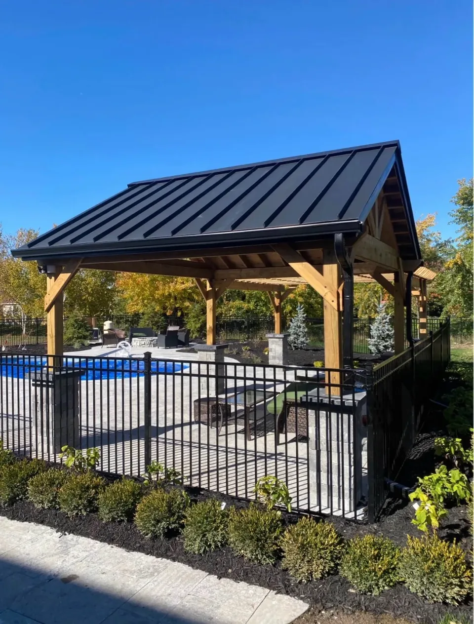Dark metal roof above a timber pavilion beside a fenced pool