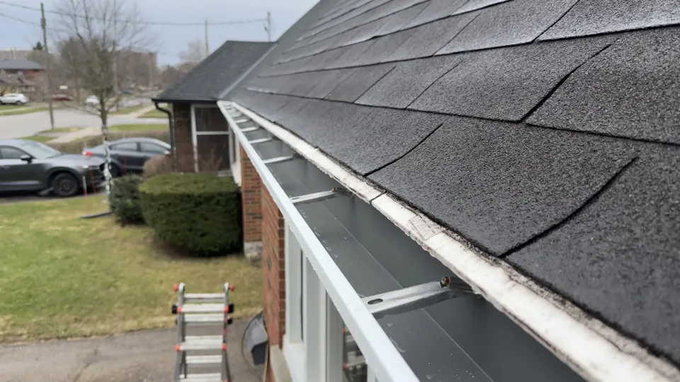 Open eavestrough running beside a shingled roof edge