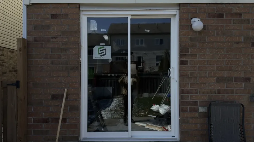 White sliding patio door in a brick wall, with a work stand beside it